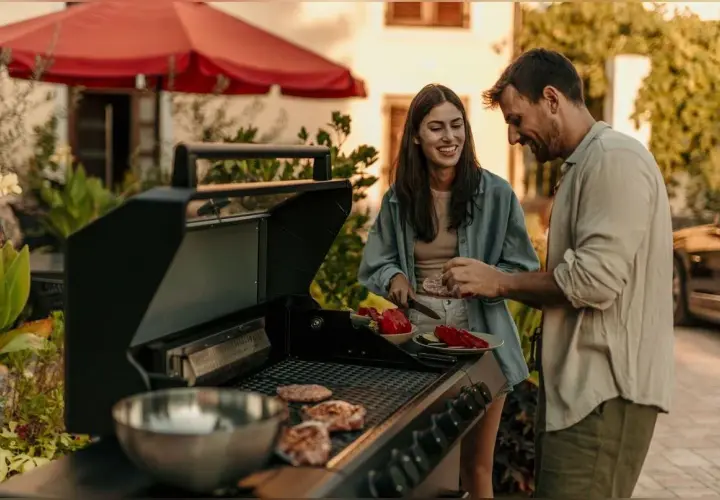 Un couple prépare une soiree barbecue party. Des steaks cuisent sur le grill pendant qu'ils coupent des légumes.