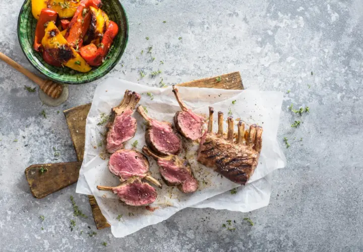 Un délicieux carré d'agneau au barbecue, coupé en côtelettes rosées, servi avec des poivrons grillés.