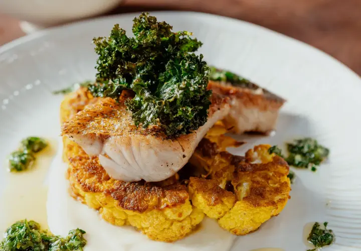Poisson grillé sur un lit de chou-fleur plancha, garni de kale croustillant et d'une sauce verte.