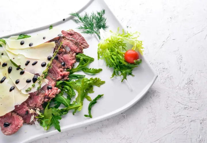Délicieuse tagliata de boeuf, finement tranchée, garnie de copeaux de parmesan, de roquette fraîche et d'une touche de vinaigre balsamique.