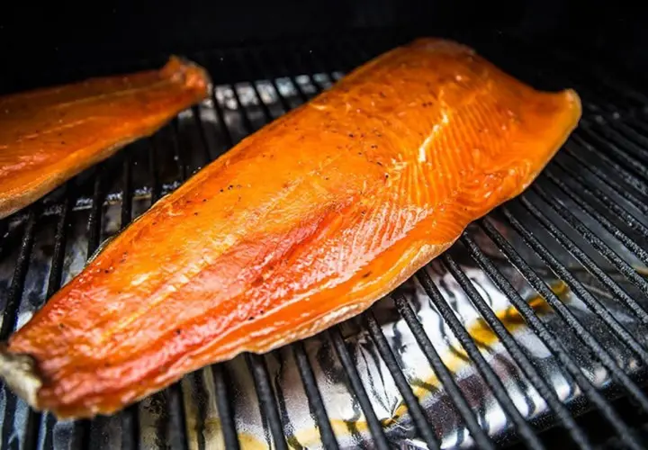 Deux filets de saumon orangés, assaisonnés de poivre, reposent sur une grille. Le temps de fumage à froid est presque terminé.
