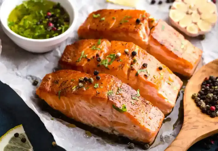 Trois pavés de saumon fumé, parsemés de poivre, accompagnés d'une sauce verte et d'une tête d'ail. Une recette parfaite pour une marinade pour saumon fumé.