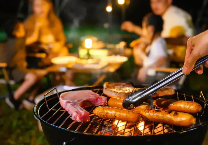 Une famille profite d'un barbecue en soirée. Des saucisses et une côte de porc cuisent sur le gril, la température de cuisson saucisse barbecue est parfaite.
