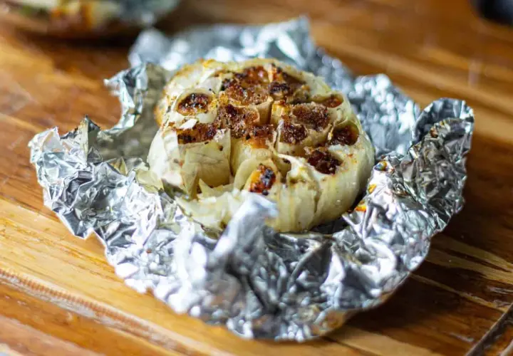 Ail au barbecue, rôti à la perfection dans du papier d'aluminium, prêt à être pressé sur du pain grillé.