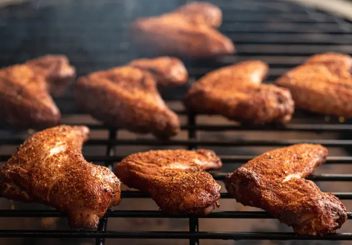 Ailes de poulet marinées pour barbecue, grillées à la perfection, dégageant une fumée alléchante.