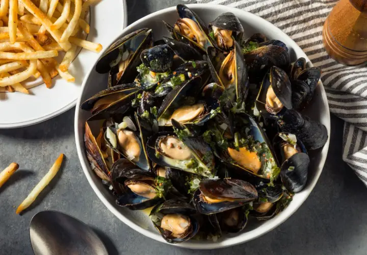 Un plat généreux de moules au feu de bois, parsemées d'herbes fraîches et servies avec des frites croustillantes.