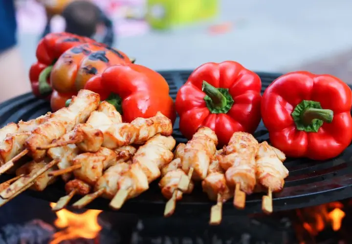 Brochettes de poulet et poivrons rouges sur un barbecue, éclairés par la lumière des flammes.