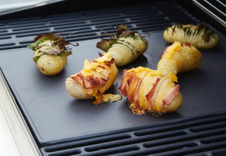Pommes de terre Hasselback garnies de lard et de fromage, prêtes à cuire sur un barbecue électrique.