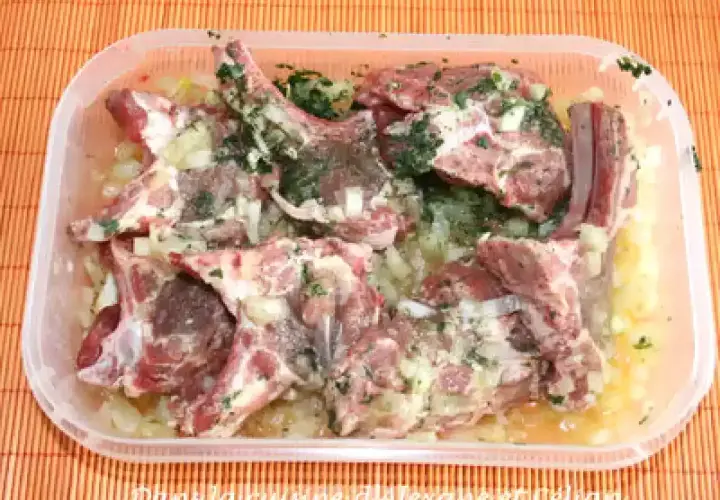 Côtelettes d'agneau crues dans une marinade à l'oignon et aux herbes, prêtes pour une recette de marinade agneau barbecue.