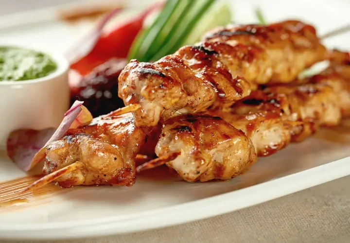Délicieuse brochette de poulet grillée, servie avec une sauce verte et des légumes croquants. Un plat savoureux et coloré.