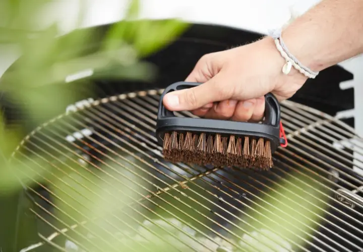 Maintenant, faut il huiler la grille du barbecue ? Une main nettoie la grille avec une brosse.
