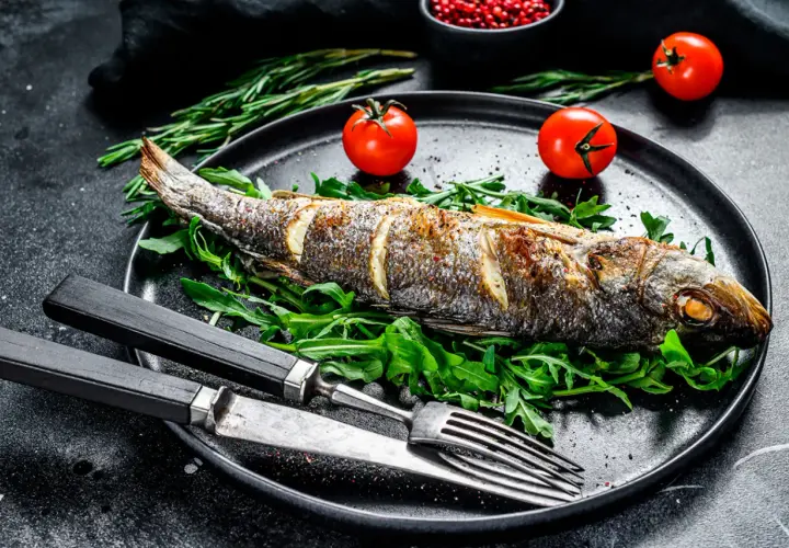 Poisson entier au barbecue, servi sur un lit de roquette avec des tomates cerises et des herbes.
