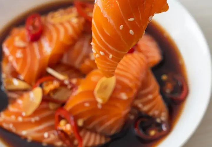 Un morceau de saumon est soulevé d'une marinade foncée avec des piments rouges et de l'ail. Parfait pour une marinade poisson plancha.