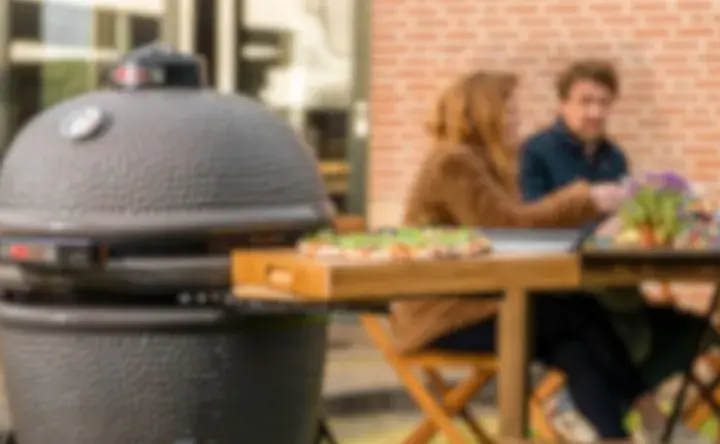 Un couple profite d'un repas en plein air avec une pizza sur une planche en bois à côté d'un barbecue kamado.