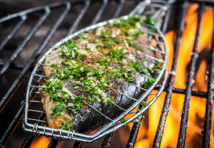 Poisson entier assaisonné d'herbes et d'épices, sur une grille de barbecue avec des flammes vives. Le temps de cuisson du poisson au barbecue est crucial pour un résultat parfait.