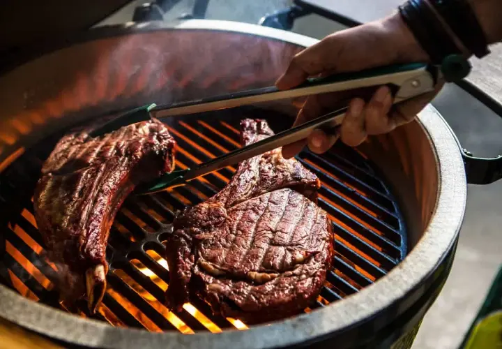 Deux côtes de bœuf savoureuses sur un barbecue à gaz, prêtes pour le temps de cuisson idéal. La chaleur intense des flammes caramélise la viande.