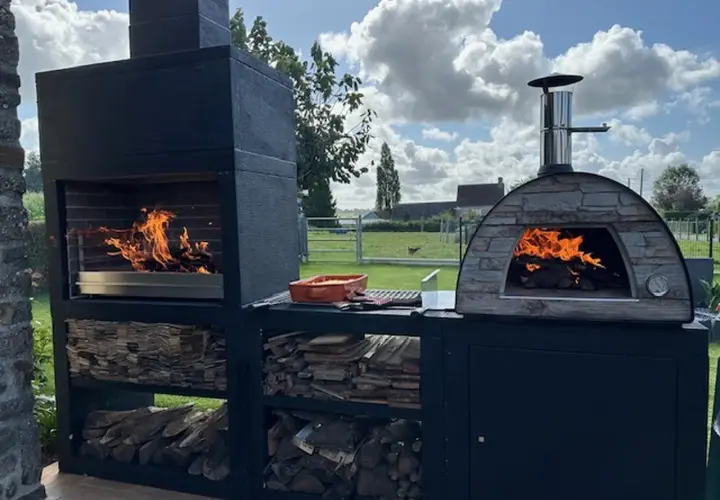 Un grand barbecue et un four à pizza en pierre sont prêts à preparer barbecue. Le feu crépite dans les deux, promettant un repas convivial en plein air.