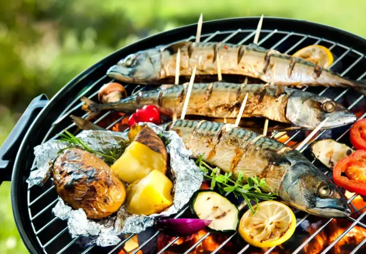 Trois poissons maquereaux grillés sur un barbecue, accompagnés de pommes de terre en papillote, de tomates et de citrons. Un délice de poisson barbecue en plein air.