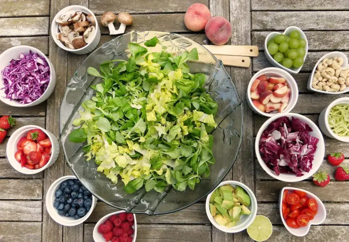 Préparation d'une salade barbecue : laitue, chou rouge, fraises, myrtilles, framboises, avocat, tomates cerises, pêches, raisins, noix de cajou, champignons et chou vert.