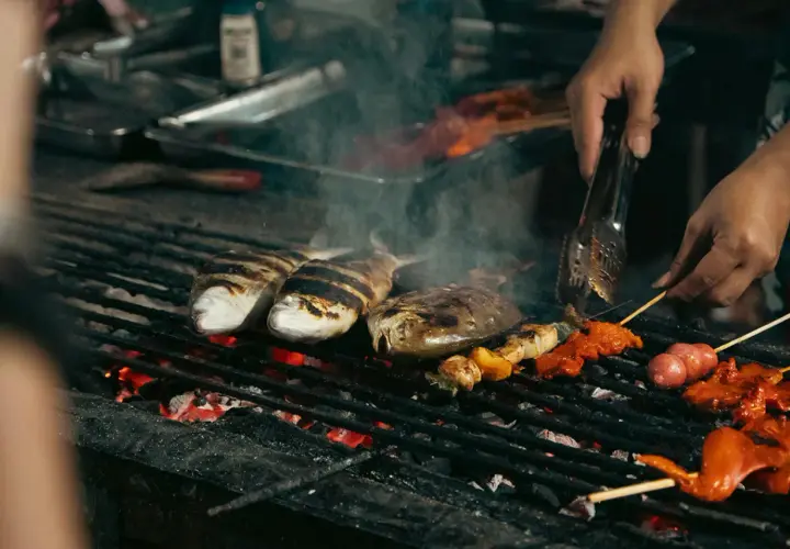 Poissons et brochettes marinés cuisent sur un gril incandescent, dégageant une fumée alléchante. Un vrai bar au barbecue !