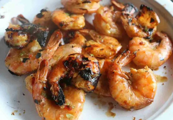 Grosses crevettes bbq, grillées à la perfection, avec des marques de cuisson foncées et une sauce savoureuse.