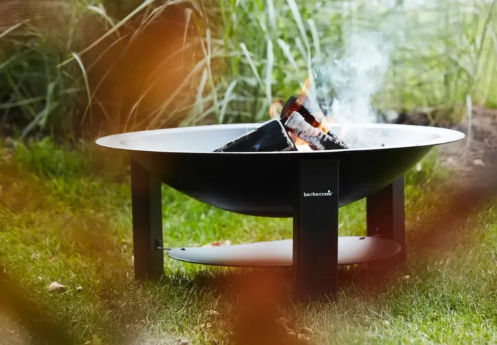 Un brasero Barbecook est prêt à allumer, avec des flammes dansantes et de la fumée s'élevant dans l'air.