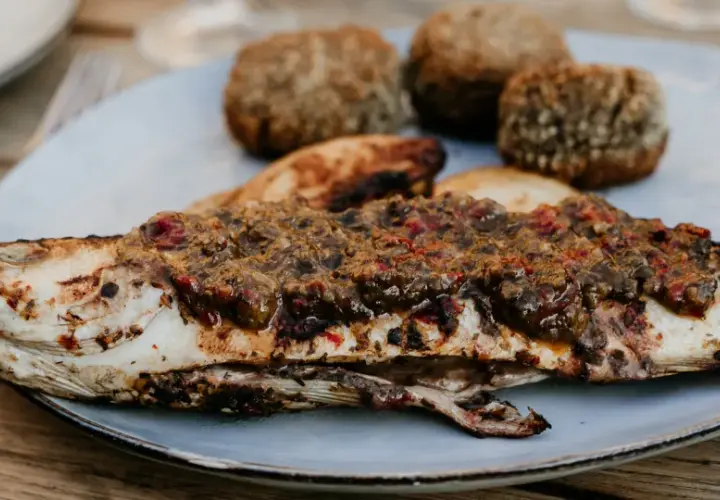Un loup au barbecue, savamment garni d'une sauce aux herbes et tomates, accompagné de petites boules de pain croustillantes.