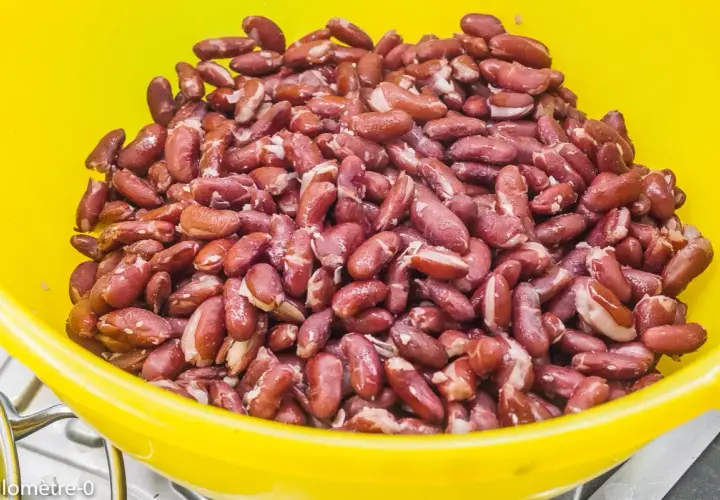 Gros plan sur des haricots rouges dans un bol jaune, prêts pour la cuisson. Ils sont brillants et humides, promettant un plat savoureux.