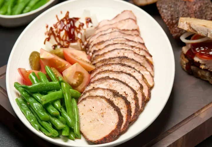 Tranches de longe de porc fumé, accompagnées de haricots verts, tomates, cornichons et oignons. Un délice fumé à savourer.