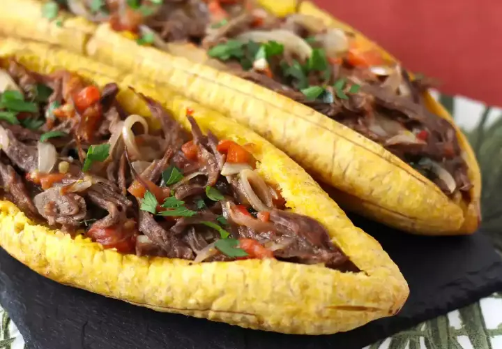 Deux bananes plantain farcies d'un ragoût de bœuf effiloché, d'oignons et de tomates, garnies de persil frais.