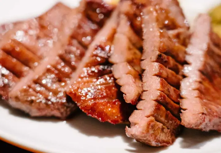 Tranches de langue de bœuf grillée, tendres et juteuses, servies sur une assiette blanche.