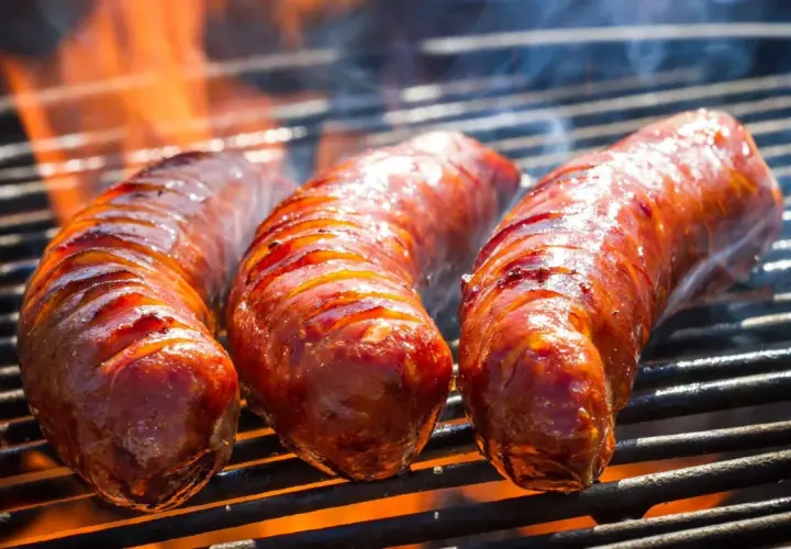 Trois saucisses de bœuf grillent sur un barbecue, leurs jus pétillent sous les flammes. La cuisson saucisse de bœuf barbecue est à son apogée.