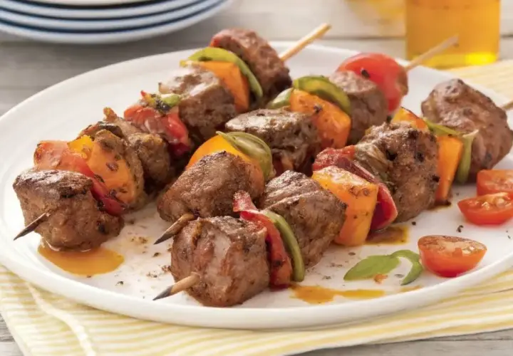 Brochettes de bœuf marinées, garnies de poivrons et tomates, servies sur une assiette blanche.