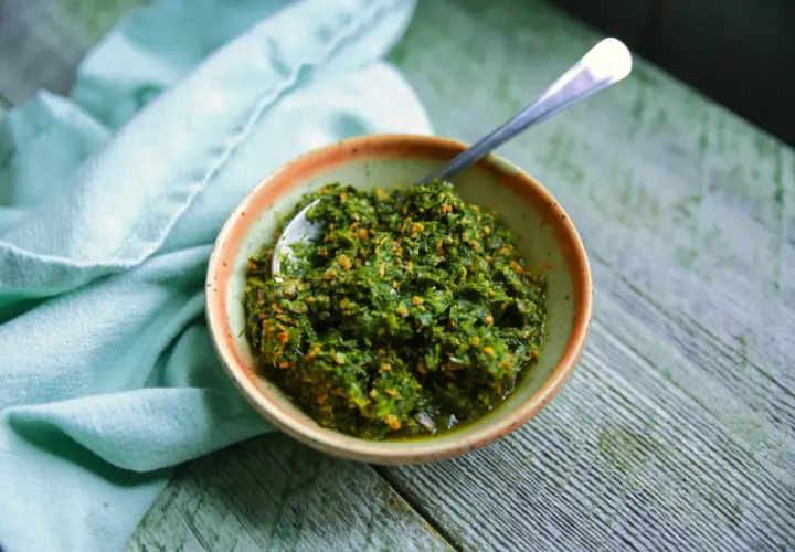 Un bol de pesto de fanes de carottes, prêt à être dégusté, avec une cuillère en argent.