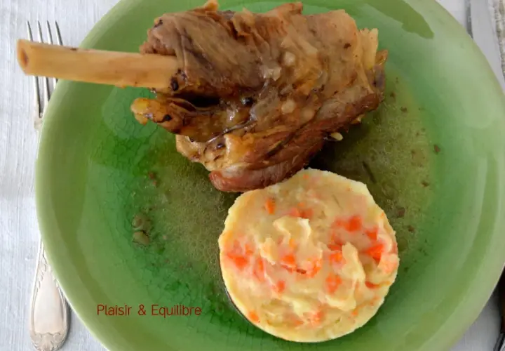 Souris d'agneau confite, tendre et savoureuse, servie avec une purée de carottes onctueuse sur une assiette verte craquelée.