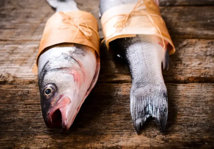 Deux poissons prêts pour le barbecue, emballés dans du papier kraft sur une table en bois rustique.