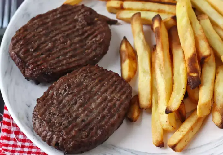 Deux steaks hachés au grill électrique, marqués de fines rayures, accompagnés d'une généreuse portion de frites dorées et croustillantes.