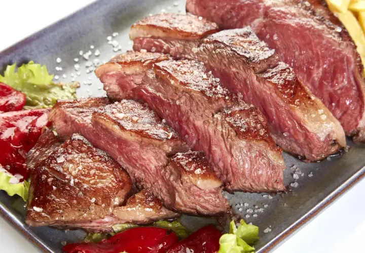 Tranches de picanha de veau juteuse, saupoudrées de gros sel, servies avec des poivrons rouges et de la laitue.