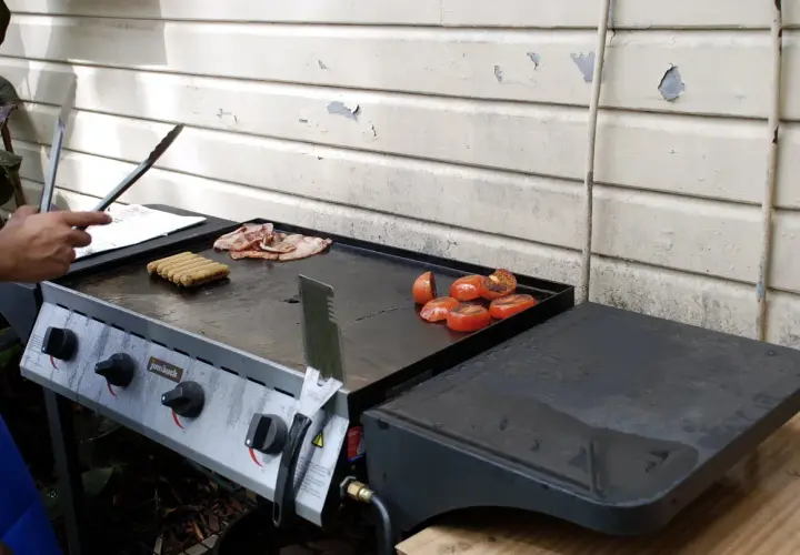 Comment allumer plancha gaz : des saucisses, du bacon et des tomates grillent sur la plaque.