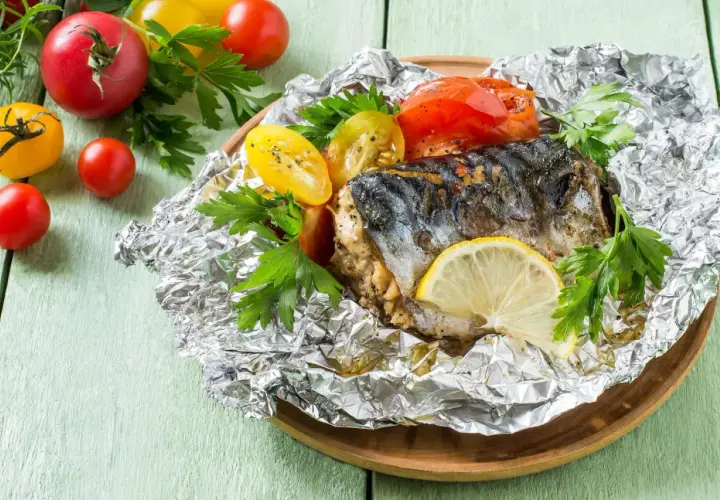 Poisson barbecue en papillote, servi avec des tomates et du persil, garni d'une tranche de citron.