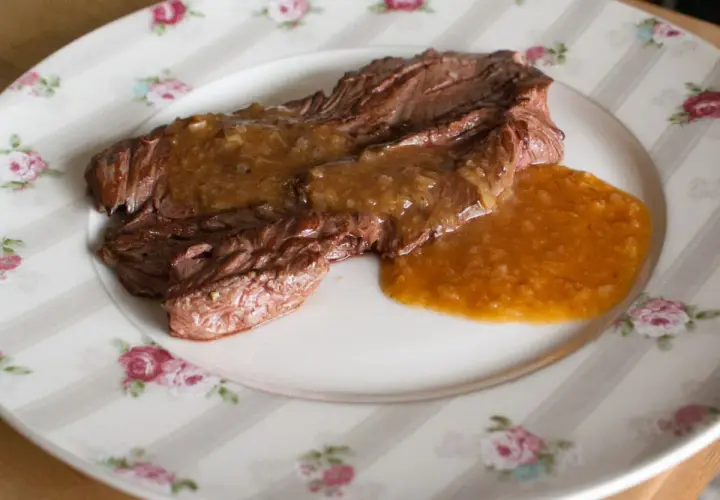 Un plat de viande tendre nappé d'une sauce onctueuse à l'échalote, servi sur une assiette à motifs floraux.