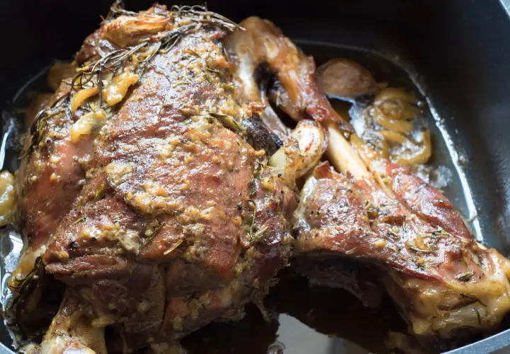 Une succulente épaule d'agneau confite, dorée et parfumée, baignant dans son jus avec des herbes et de l'ail.