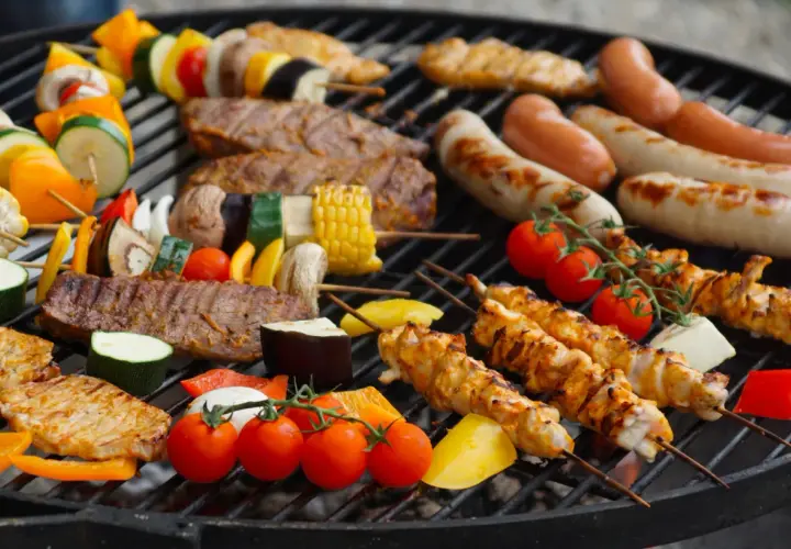Un festin de Noël en plein air : brochettes de poulet, saucisses, steaks et légumes colorés sur un barbecue.