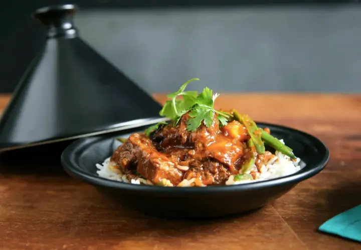 Un plat de riz blanc garni d'un ragoût de bœuf savoureux, aux haricots verts et coriandre, servi à côté d'un tajine noir. La marinade boeuf a conféré une sauce riche et appétissante.