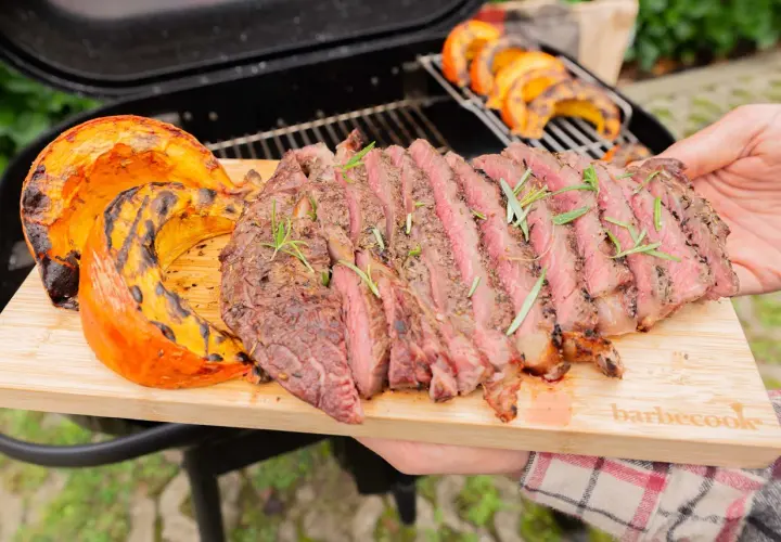 Un steak grillé et des quartiers de potimarron barbecue, servis sur une planche en bois.