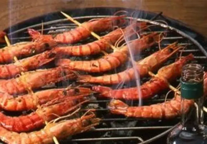 Gambas grillées sur un barbecue, fumantes et appétissantes. Une bouteille de sauce est à proximité, suggérant une délicieuse marinade pour gambas au barbecue.