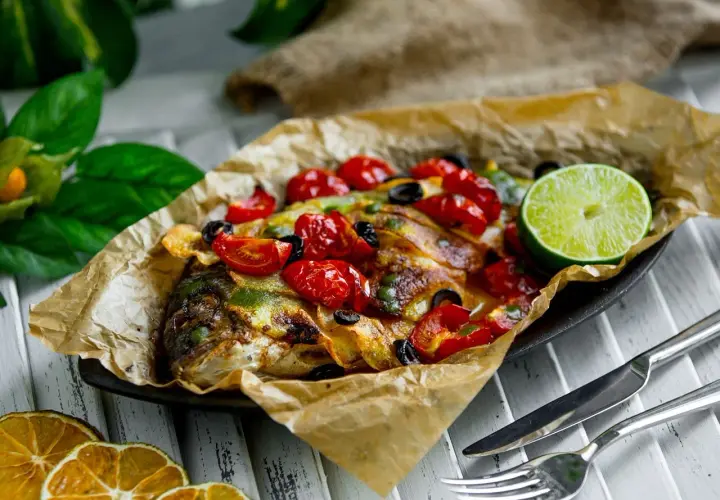 Dorade en papillote au barbecue, garnie de tomates cerises, olives et citron vert. Le temps de cuisson est parfait pour ce plat savoureux.