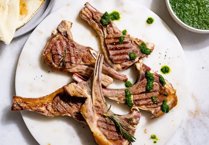 Délicieuses côtelettes d'agneau barbecue, grillées à la perfection, arrosées d'une sauce verte vibrante et garnies de romarin frais.
