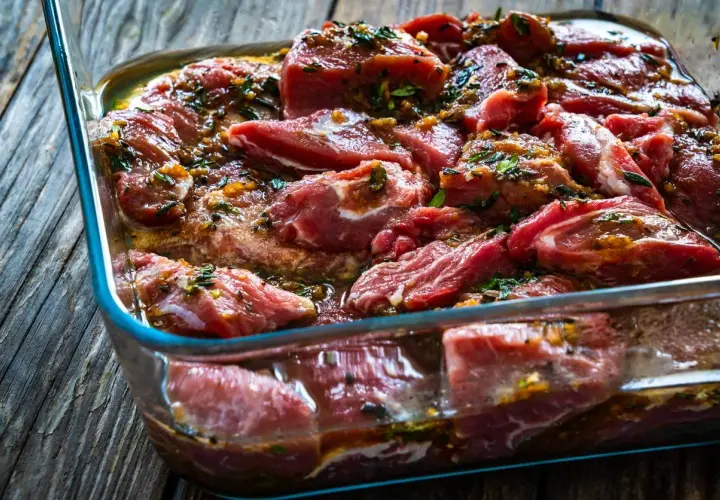 Morceaux de joue de porc marinés dans un plat en verre, prêts à être cuisinés.