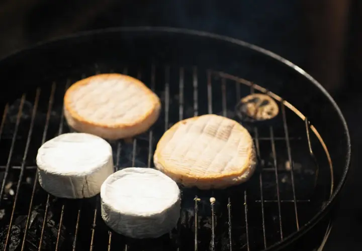 Fromages ronds, dont certains enrobés de blanc, chauffent sur un barbecue. Une idée gourmande pour un barbecue feta.